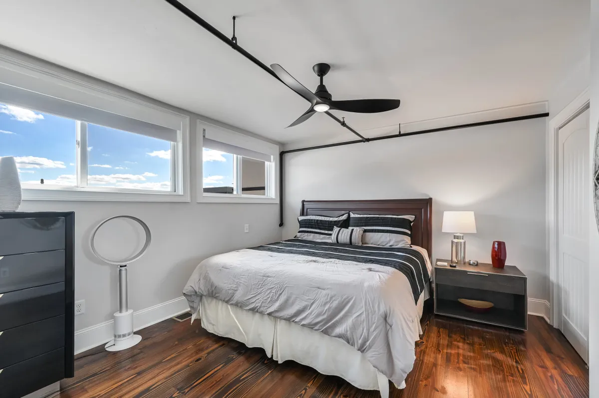 A serene king bedroom with a plush bed, ample windows letting in natural light, and a minimalist nightstand. The soft color palette and uncluttered design create a tranquil ambiance perfect for relaxation and privacy.
