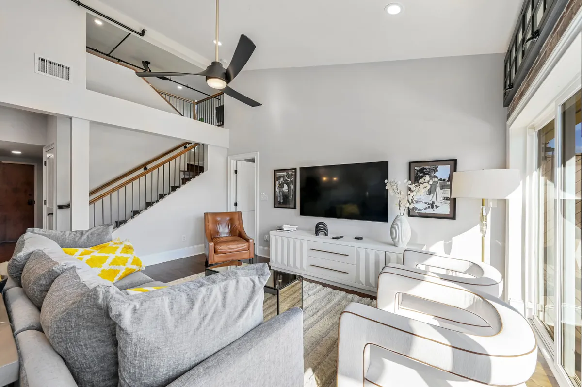 A contemporary living area with a sofa accented by a yellow pillow, a modern coffee table, a flat-screen TV, and a stylish armchair. The layout emphasizes comfort and functionality, ideal for relaxing or socializing.