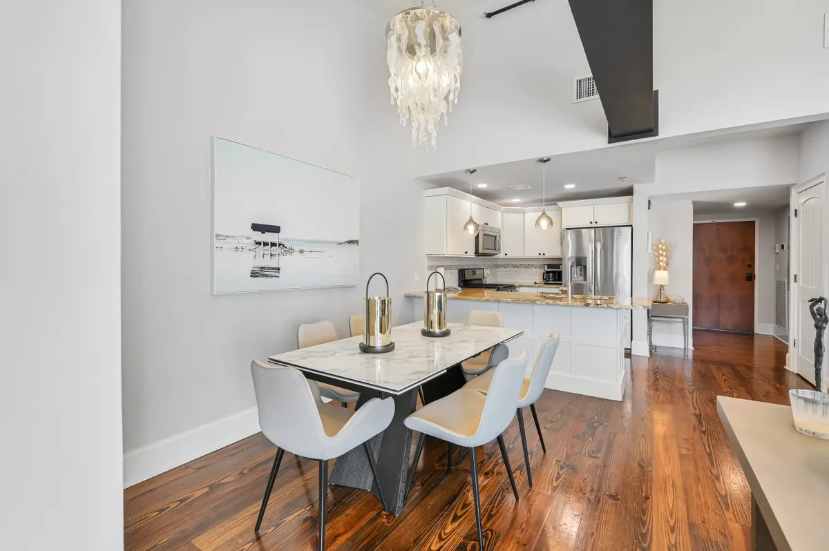 A sophisticated interior scene featuring a marble dining table set beneath a striking chandelier, with an open kitchen area visible in the background. The space is arranged for both intimate meals and lively gatherings, with modern décor and inviting seating.