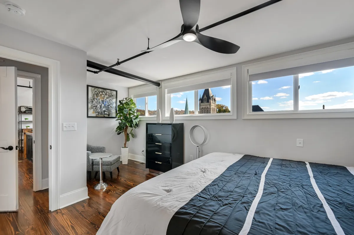 A modern king bedroom featuring a comfortable bed, large windows overlooking a scenic view, a plant for a touch of nature, artwork on the walls, and a functional dresser. The atmosphere is both contemporary and restful, with an inviting feel.
