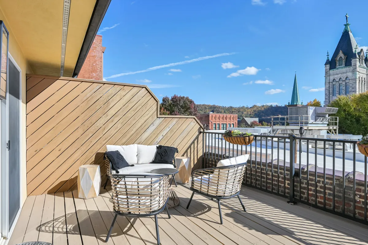 An inviting outdoor seating area set against a backdrop of downtown Asheville's cityscape. Decorative planters flank comfortable chairs and a table, while the view highlights nearby historic architecture and urban vibrancy, suggesting easy access to city life beyond the building.