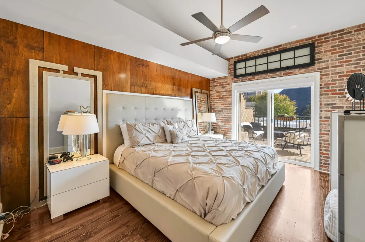 A tranquil bedroom featuring a bed, mirrors, exposed brick wall, soft lighting, and an inviting view out the window. The scene is peaceful, with a clear visual link to the outdoors.