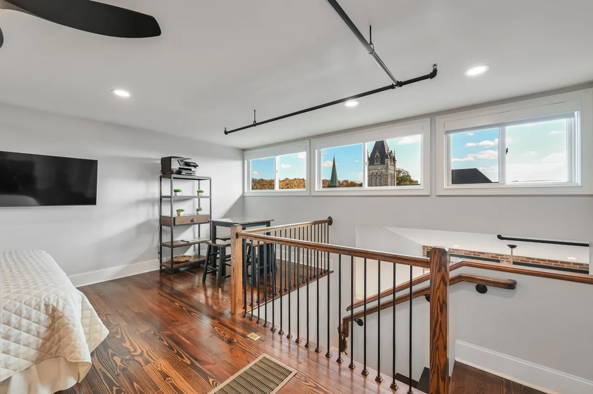 This inviting living area features large windows with panoramic views, a wooden railing, and a modern shelving unit. The abundance of natural light and cityscape outside pairs with a cozy, contemporary gathering space inside.